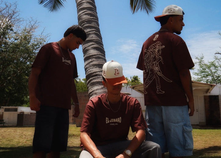 Three men in casual clothing with caps standing under a palm tree on a sunny day.